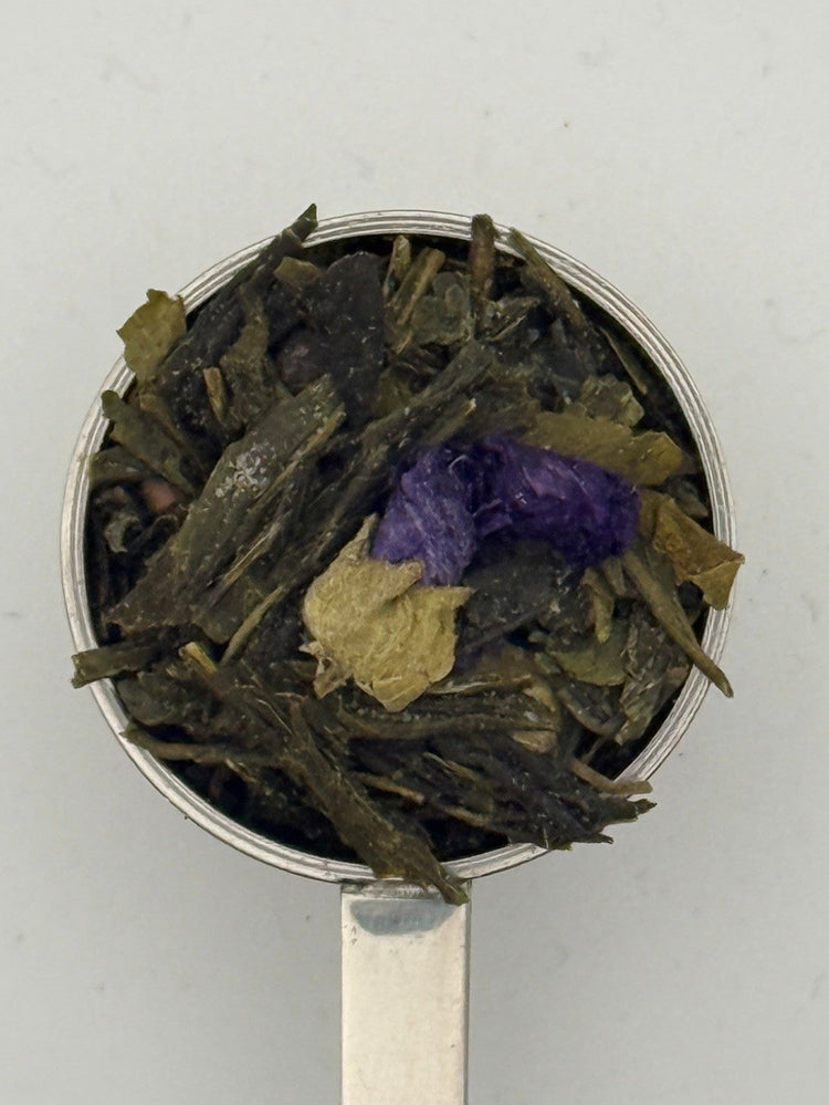 Tea leaves including green and purple elements on a metal spoon against a light gray background